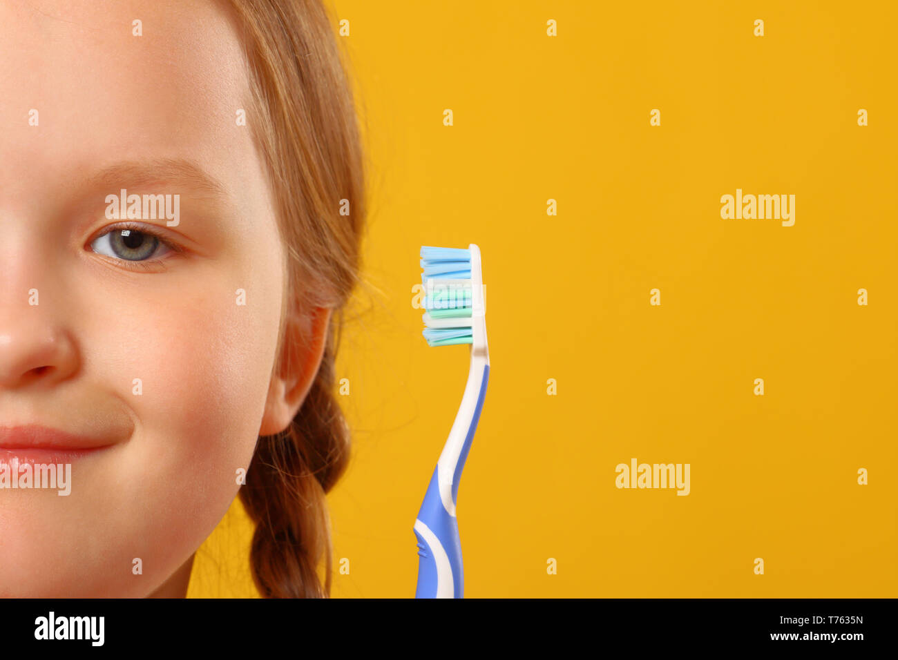 Closeup portrait of little girl's face on yellow background. holding a toothbrush. The concept of daily hygiene. Stock Photo