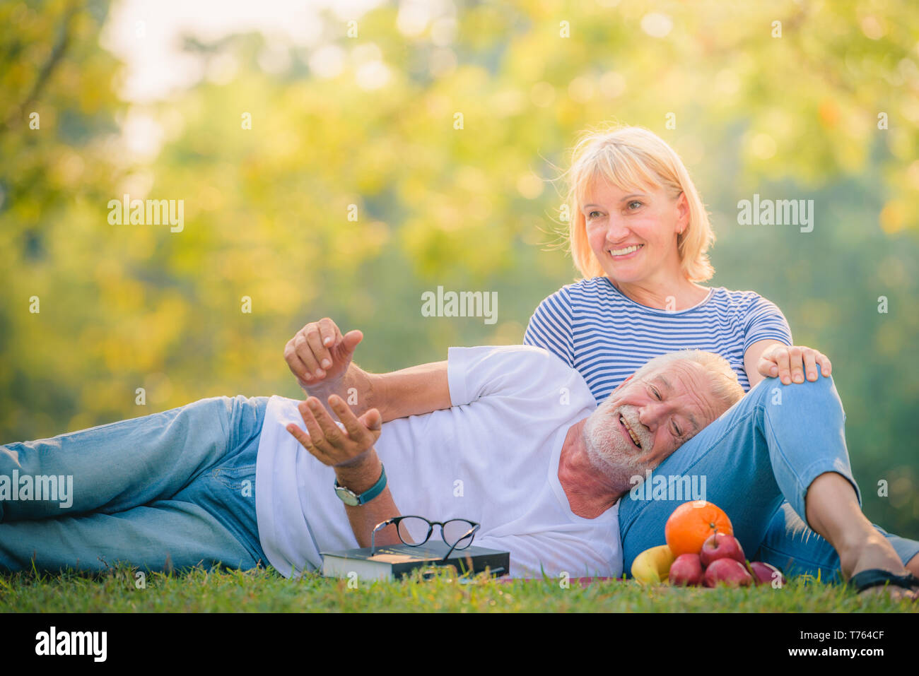 Elderly couple reading newspaper in garden at sunset. Concept couple elder love. Stock Photo