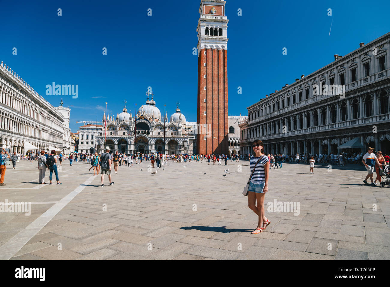 Venice, Italy - September, 9 2018: Young smiling woman tourist walking in the middle of at St. Mark's Square, Piazza San Marco with St Mark's Campanil Stock Photo