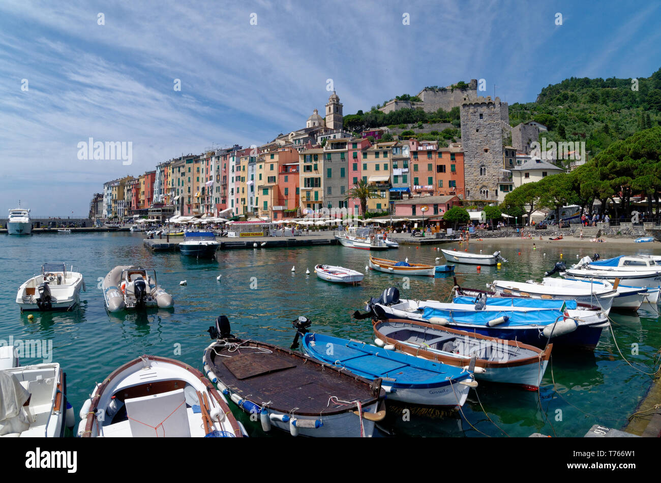 Looking across many small boats in the harbour at Porto Venere to colourful waterfront buildings, with Porta del Borgo and Doria Castle beyond Stock Photo