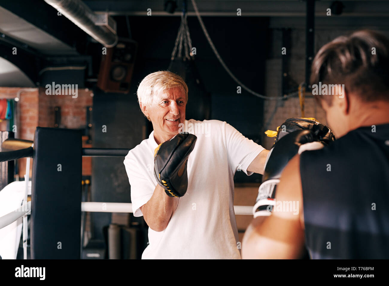 Mature boxing coach wearing punching pads training a athlete Stock