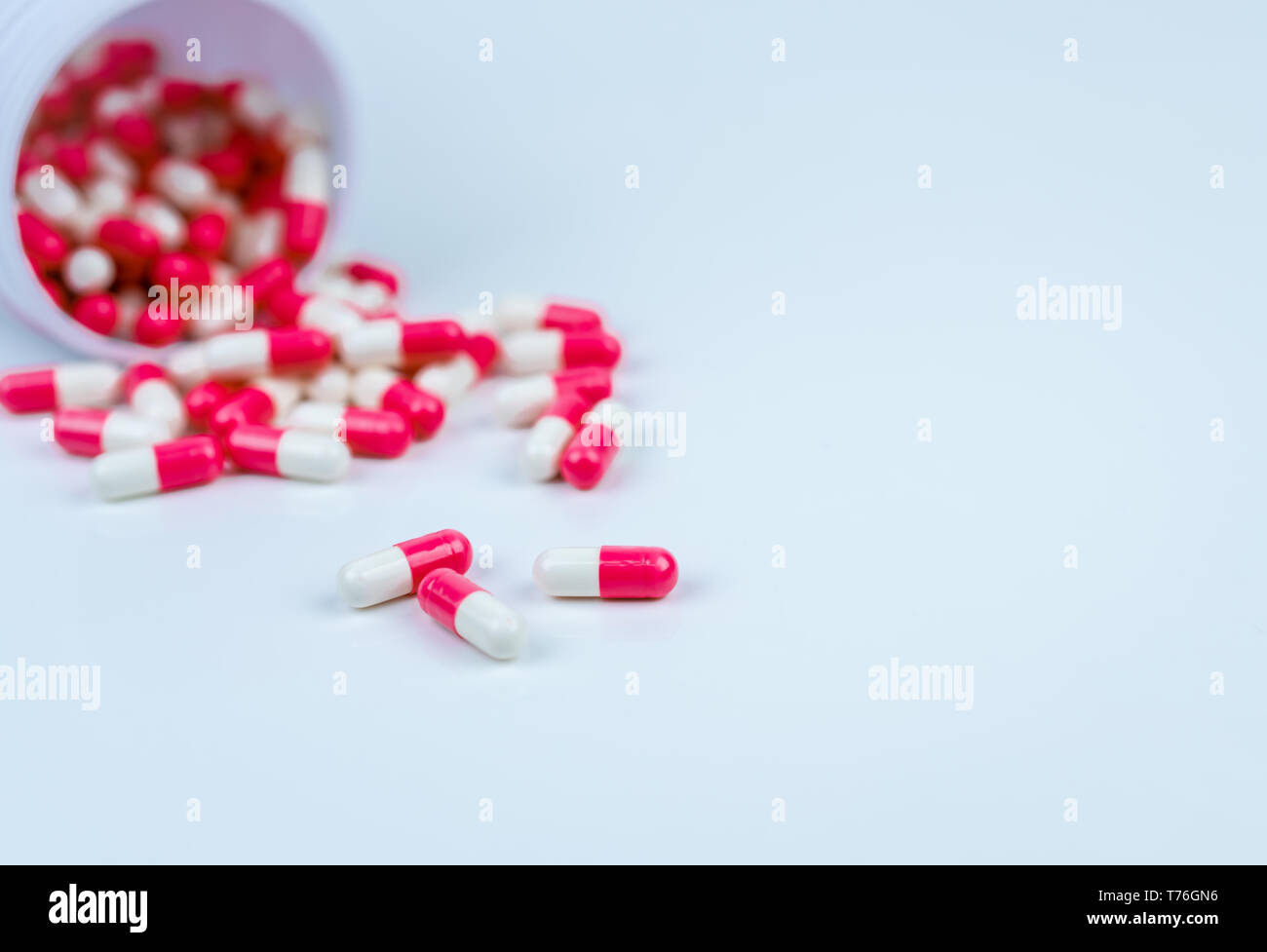 Pink and white capsules pill spilled out from white plastic bottle container. Global healthcare concept. Antibiotics drug resistance. Antimicrobial Stock Photo