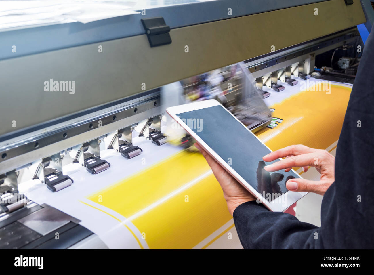 Technician touch control tablet on format inkjet printer during yellow vinyl paper Stock Photo