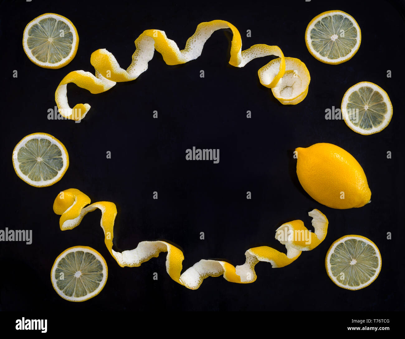 Whole and cut lemons. Frame made of lemon spiral peel, on black