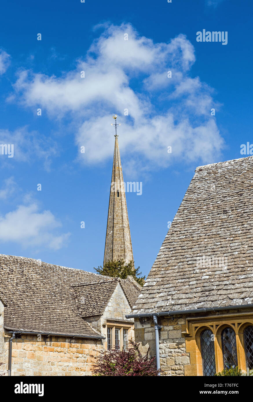 The spire of Stanton church rising between two buildings in the Cotswolds Gloucestershire England Stock Photo