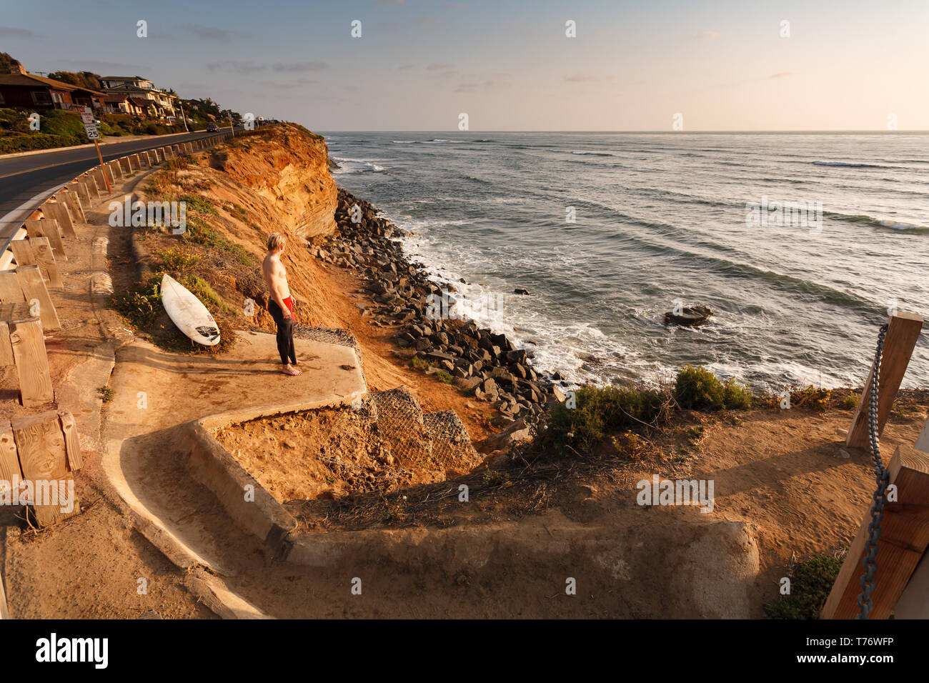 Surfer stands on cliffs above surf to watch breaks in San Diego, California Stock Photo