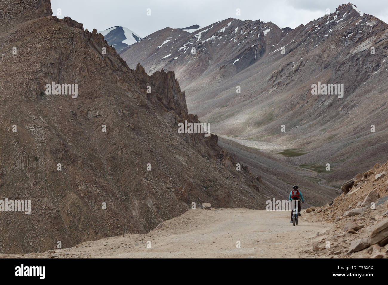 Single bike rider high in snow capped mountains rounding curve and heading down on pass through mountains to Kashmir, India on a sunny day Stock Photo