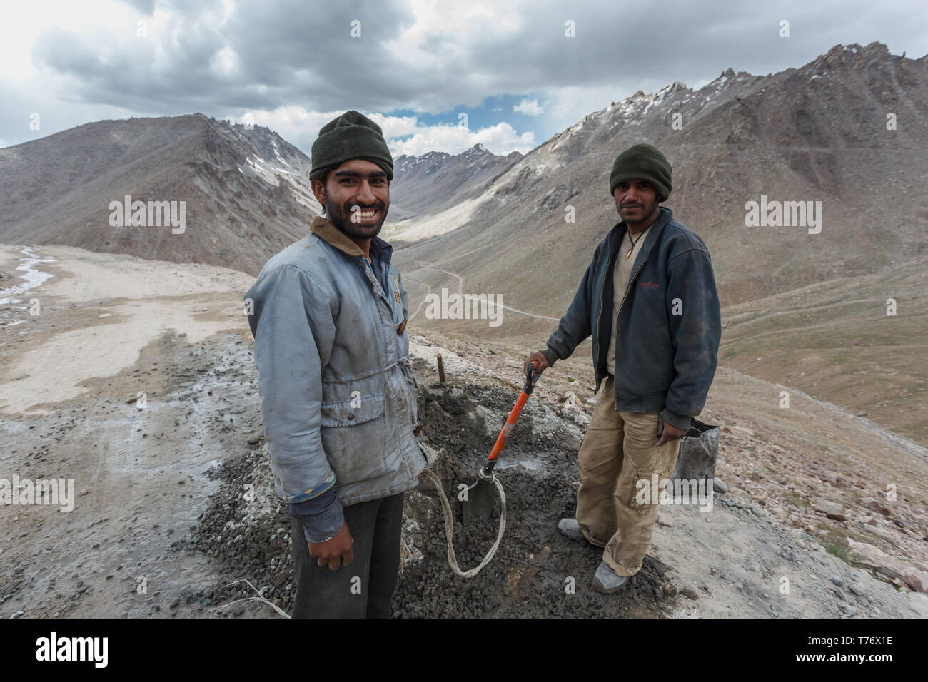 Bikers riding Mountain Biking in high Khardungla Pass, India, pass two smiling laborers repairing a patch of roadway washed out on motorway over borde Stock Photo