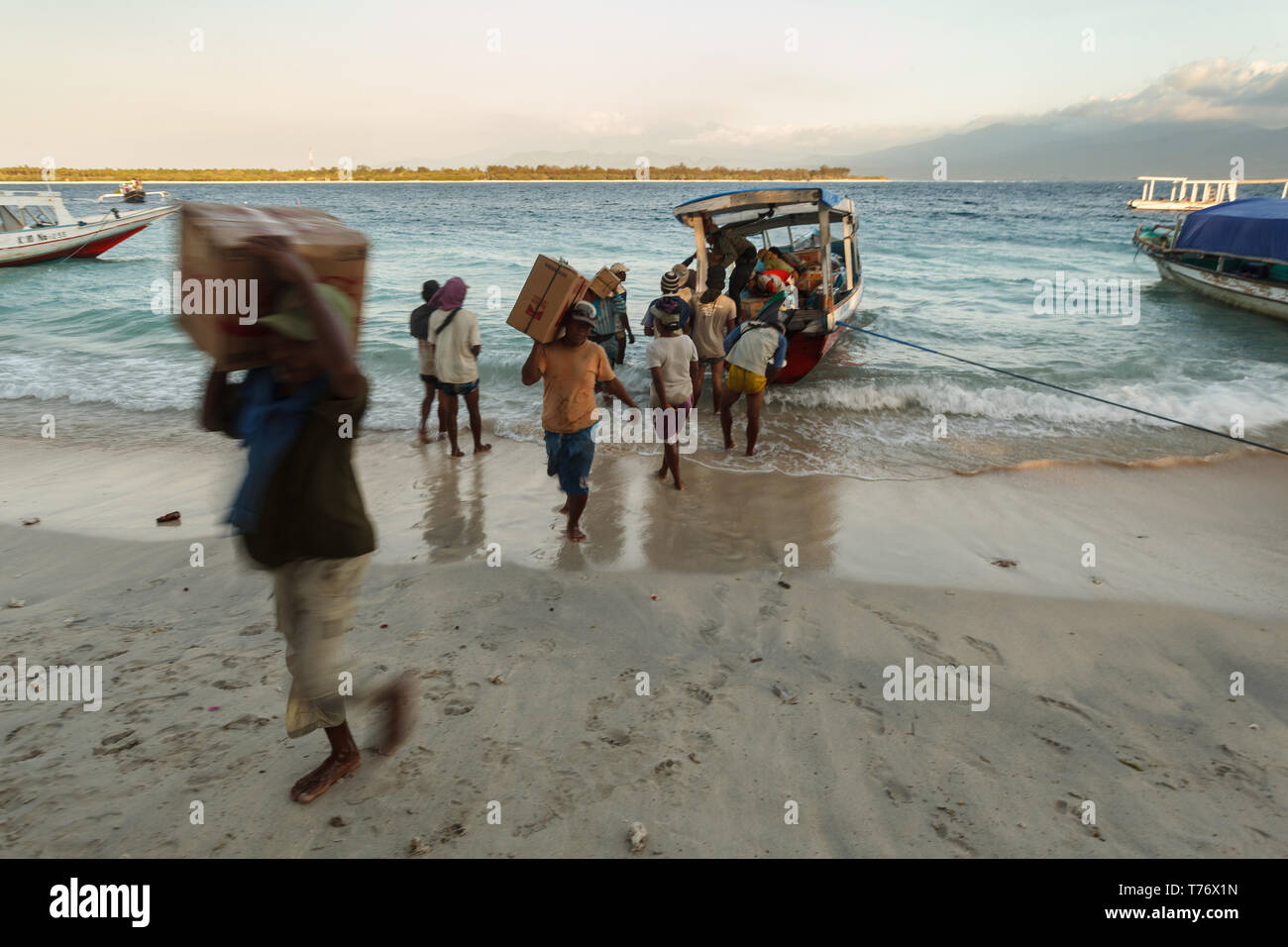Local ferry moored on beach for quick unloading of cargo and passengers who walk barefoot into water to board Stock Photo