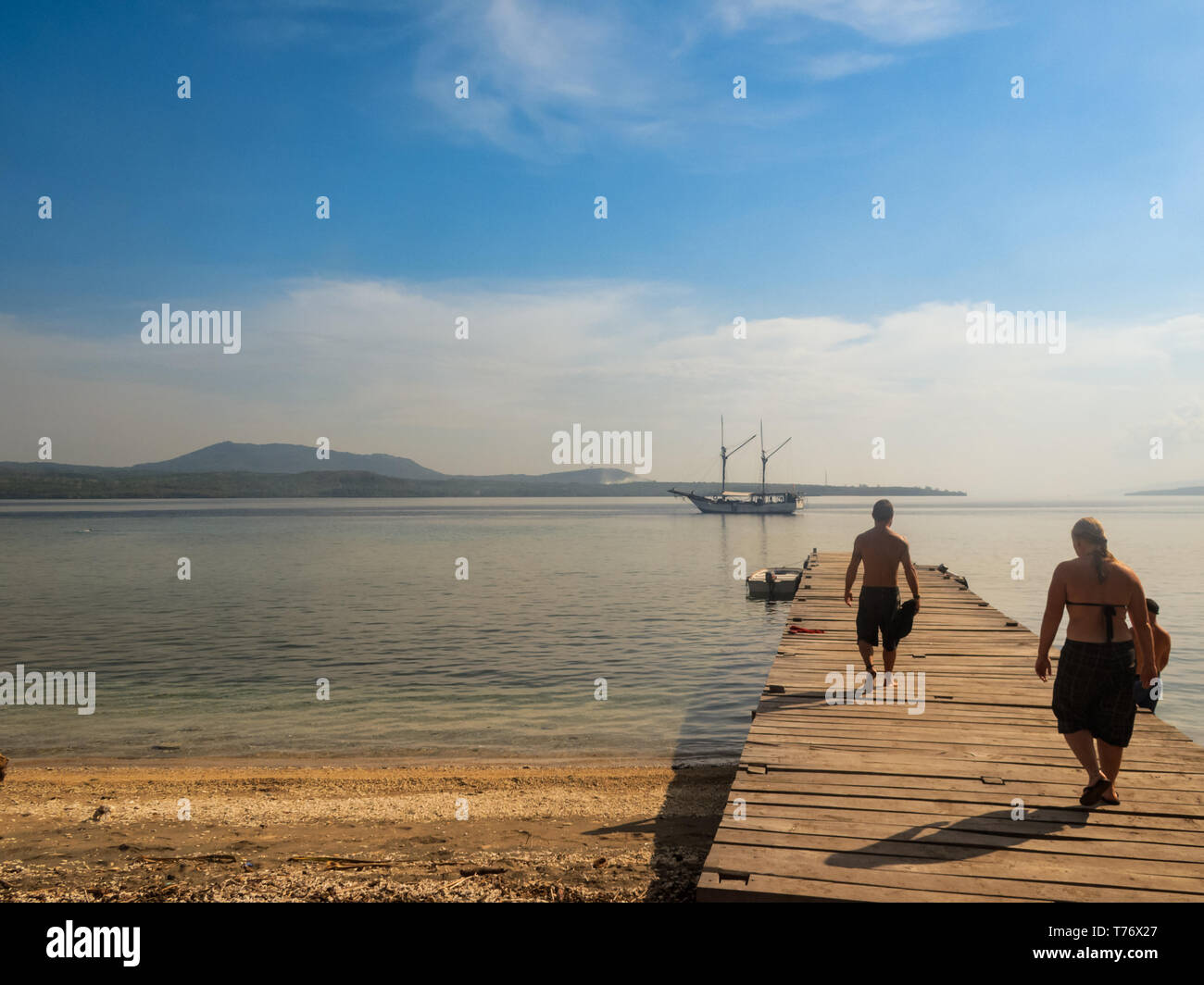 Two swimmers cross boardwalk at beach in Nussa Tenggara to get to dingy to take to moored sailboat Stock Photo