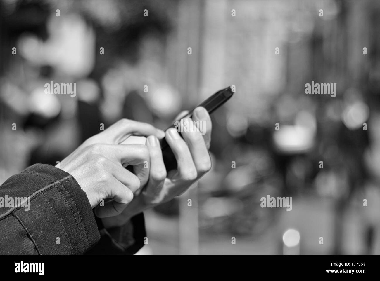 Man holding and typing on mobile phone on the street, crowd of people in background. Technology addiction. Black and white image. Stock Photo