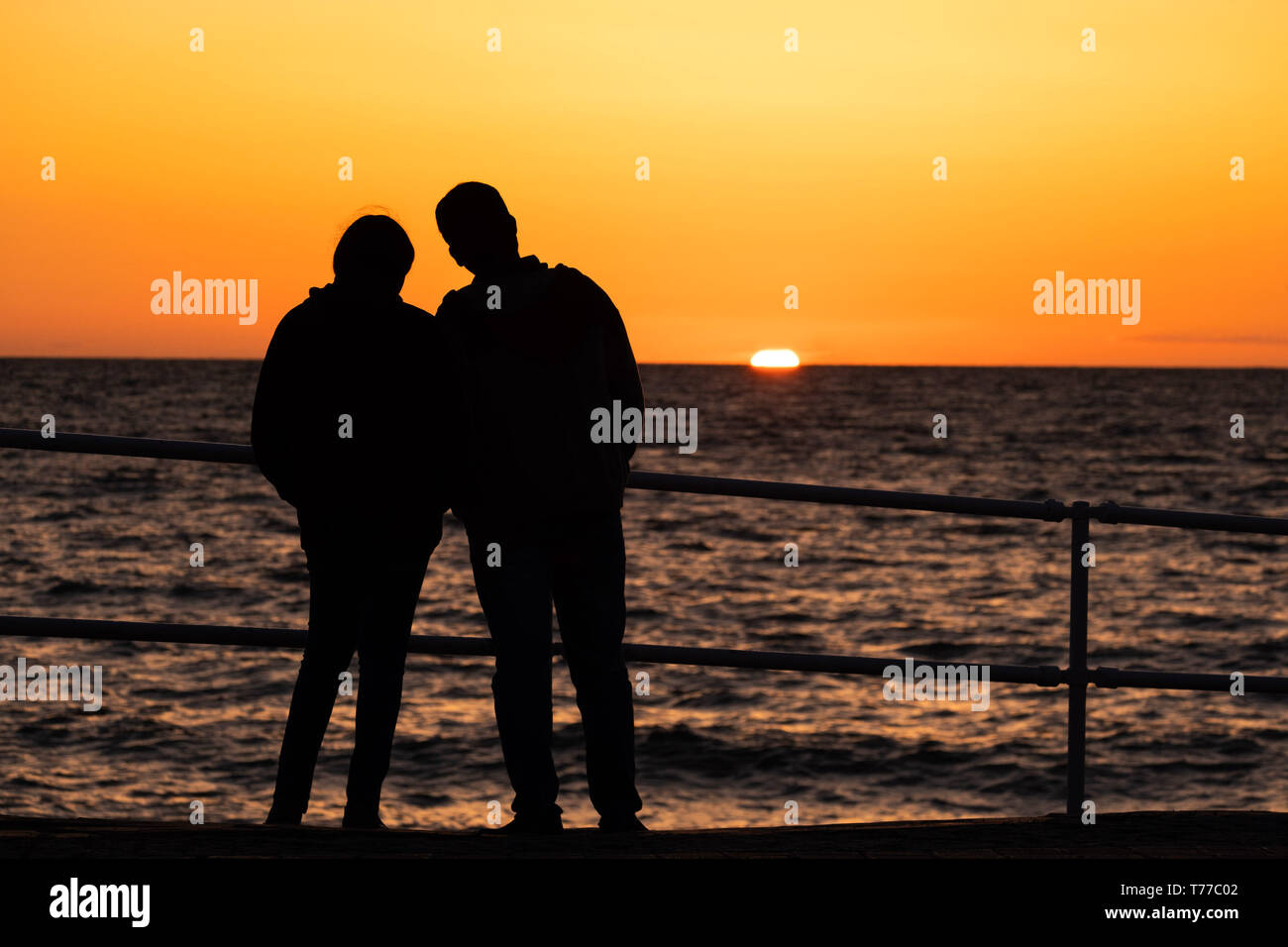 Aberystwyth, UK. 4th May, 2019.   UK Weather: People watching a glorious sunset over Cardigan Bay in Aberystwyth, at the end of a day of bright sunshine, blue skies but a bitingly cold northerly wind, on the Satrurday evening of the early May Bank Holiday weekend  photo credit Keith Morris / Alamy Live News Stock Photo