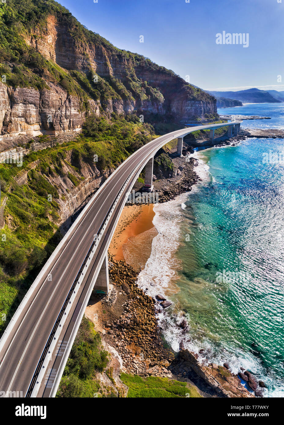 Modern highway of Sea CLiff Bridge around steep sandstone cliffs on Australian pacific coast - part of the Grand Pacific drive. Vertical aerial panora Stock Photo
