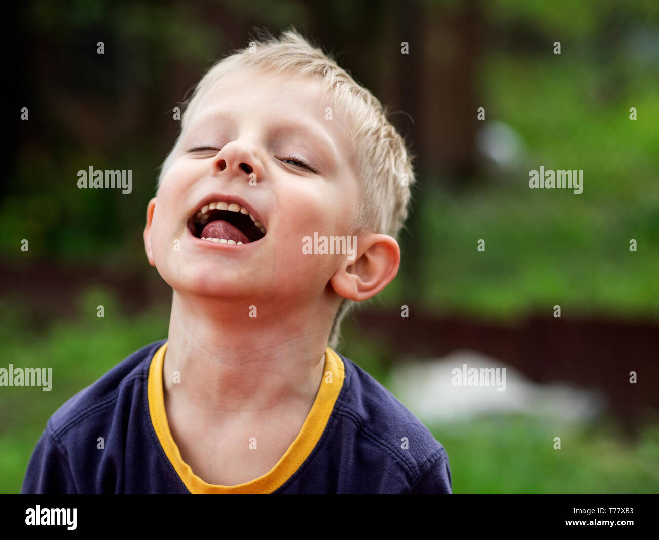 Expressive Caucasian blond little boy opened his mouth and looking at the camera from behind half-closed eyelids Stock Photo