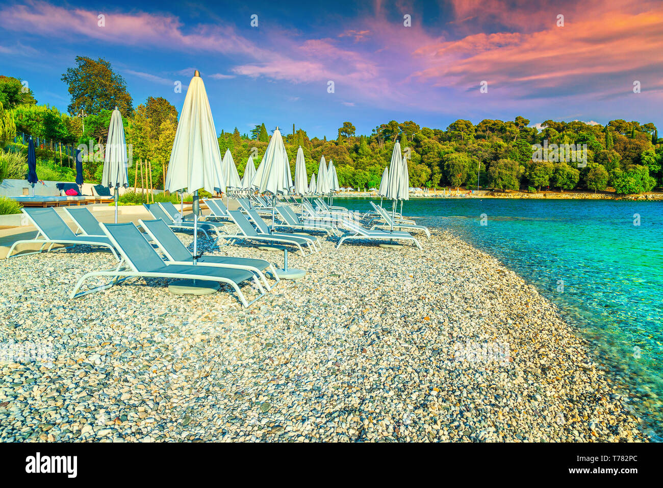 Beautiful travel and vacation destination. Picturesque gravel beach and seashore. Sun loungers and beach umbrellas at sunset on the beach, Rovinj, Ist Stock Photo