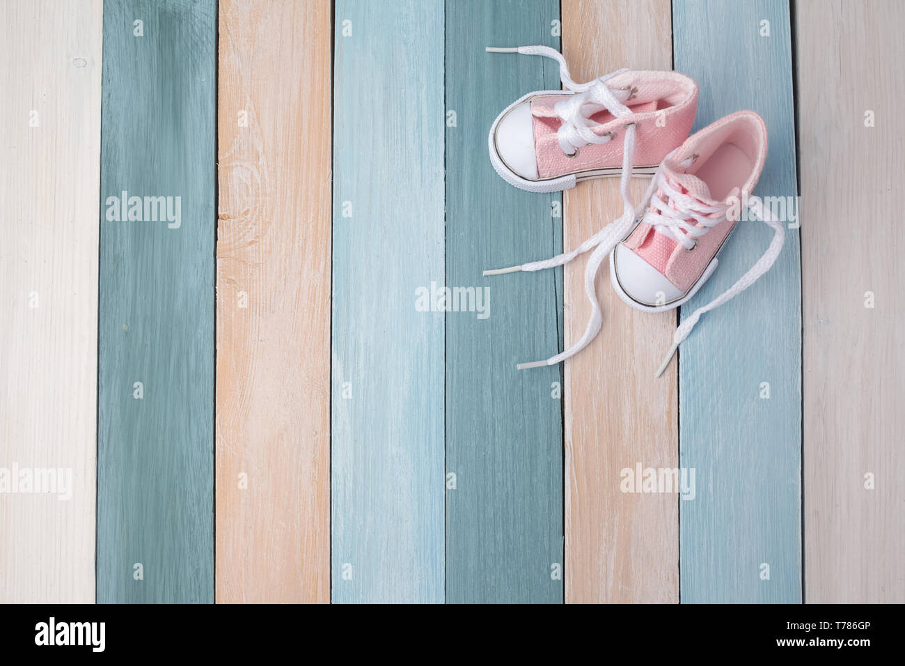 Cute tiny baby shoes on a pastel wooden background with space for text