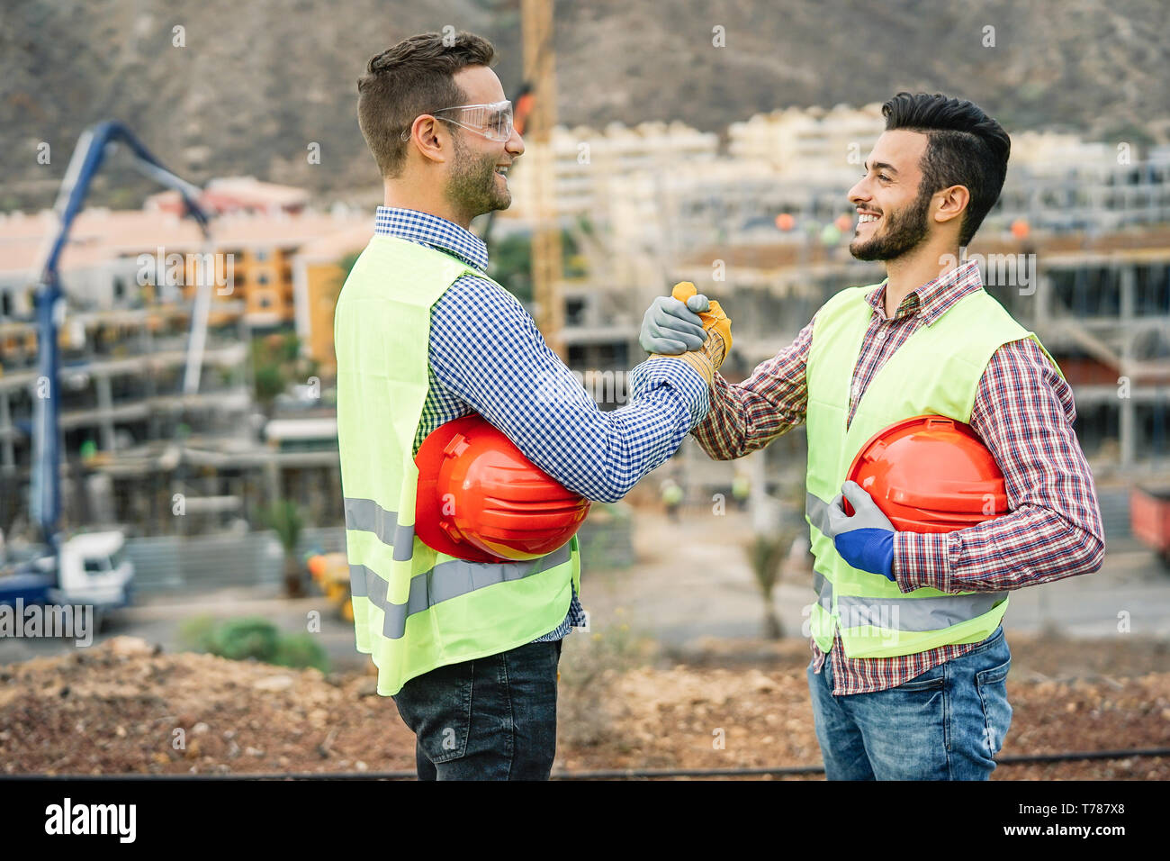 Young builders shaking hands making an agreement on costruction site - Workers reaching a deal and laughing Stock Photo