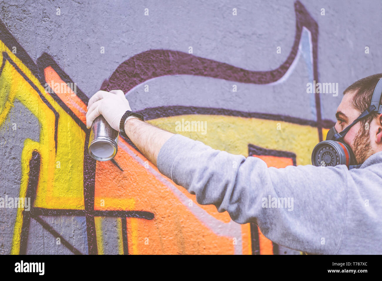 Street artist painting with a color spray can a graffiti on a wall ...