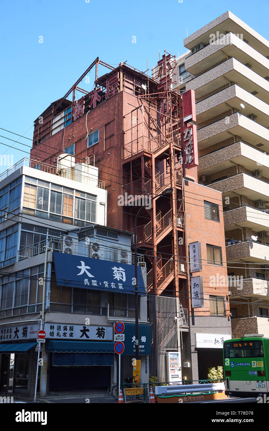 Old and new hotels in the Asakusa district of Tokyo. The red brick capsule hotel has a fire escape stairwell leading down the street side face. Stock Photo
