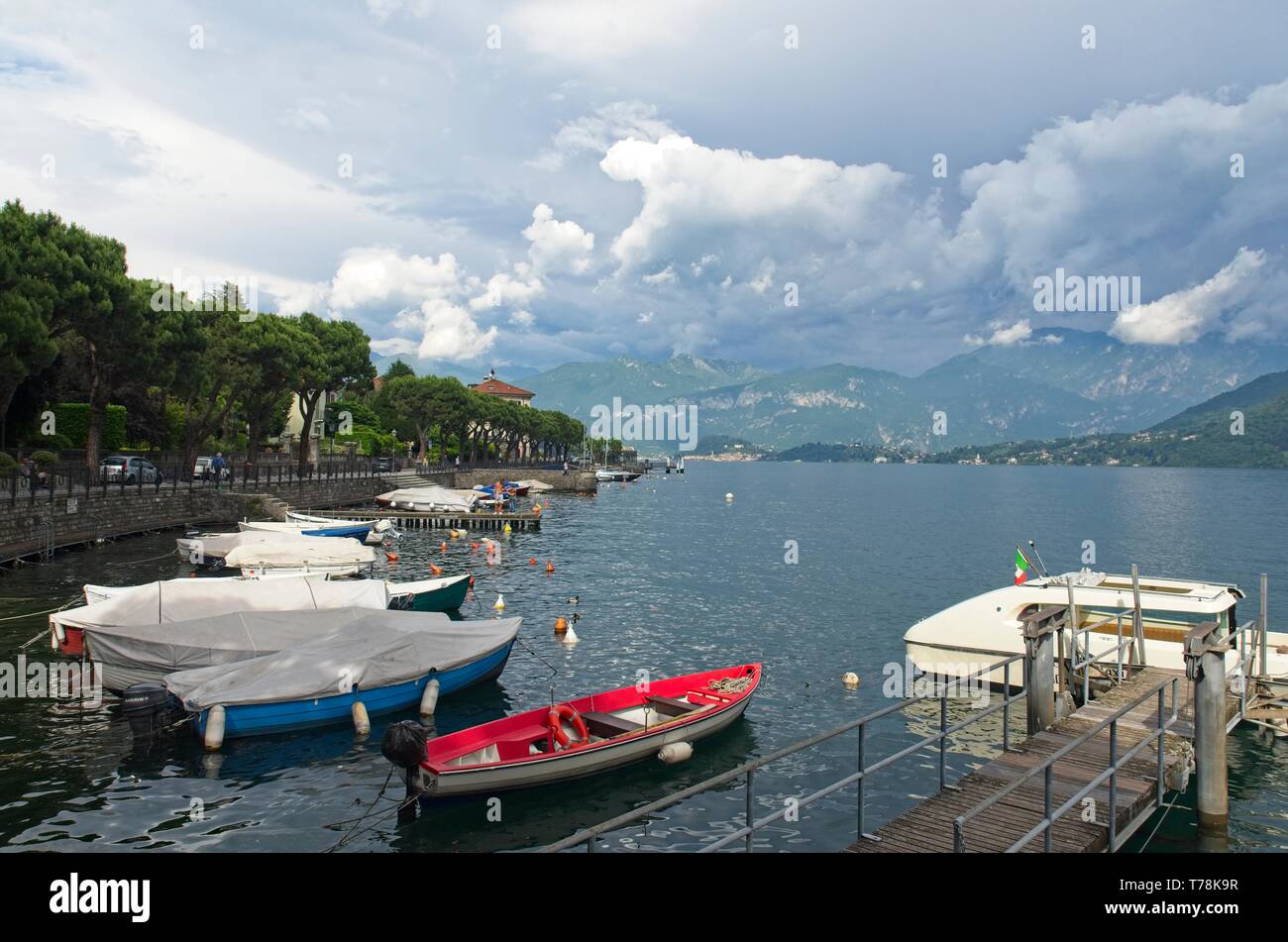 A view across Lenno harbour across Lake Como towards Bellagio in the distance with mountains beyond, under a moody grey sky Stock Photo