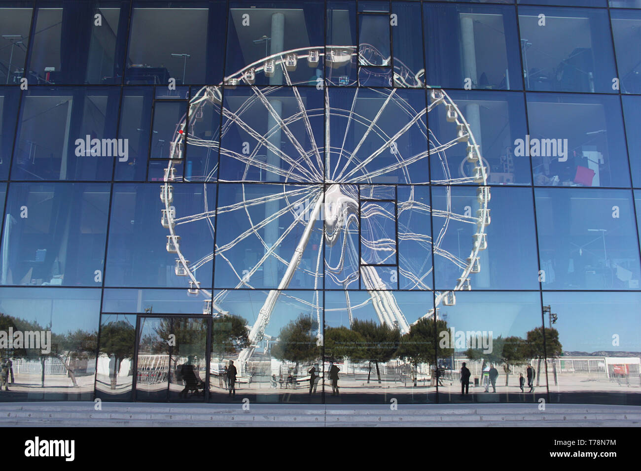 A big wheel reflected in the glass windows of Marseille's new MuCEM building, designed by Rudy Ricciotti Stock Photo