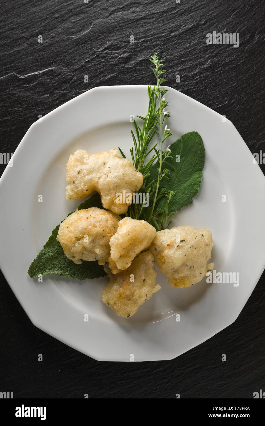 Un piatto di frittelle di baccalà, con salvia e rosmarino. [ENG]  A dish of fried salted codfish, with sage and rosemary. Stock Photo