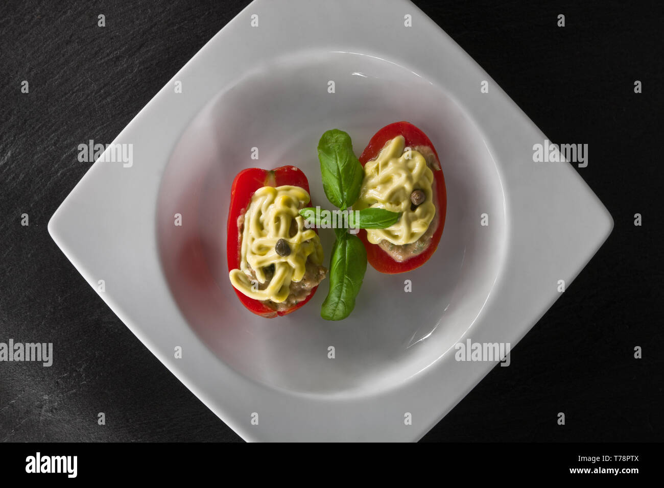 Un piatto di pomodori ripieni con guarnitura di maionese e foglia di basilico. [ENG]  A dish of filled tomatoes covered with mayonnaise and basil leav Stock Photo