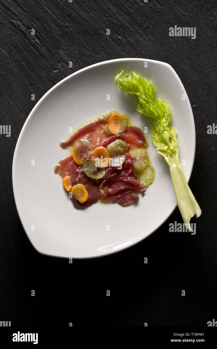 Un piatto di carpaccio di carne con guarnizione di sedano e carote.  [ENG] A plate of carpaccio (thinly sliced raw meat) decorated with carrots and ce Stock Photo