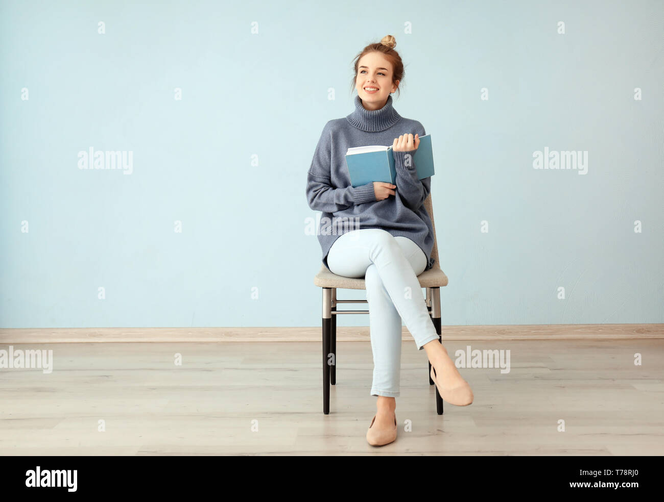 Young woman with book sitting on chair near color wall Stock Photo - Alamy