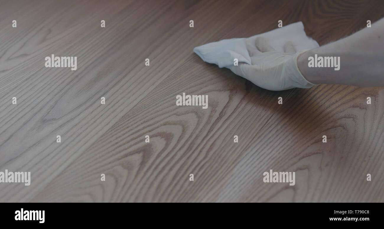 Closeup man in gloves cleaning ash wood floor with wet cloth, shallow