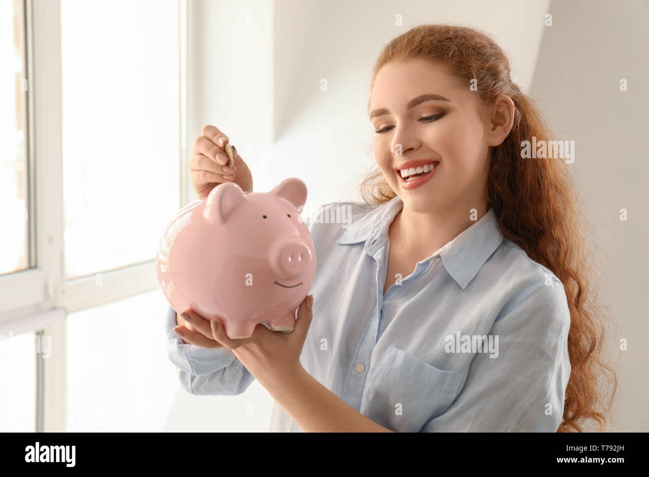 Woman putting coin into piggy bank indoors. Money savings concept Stock ...