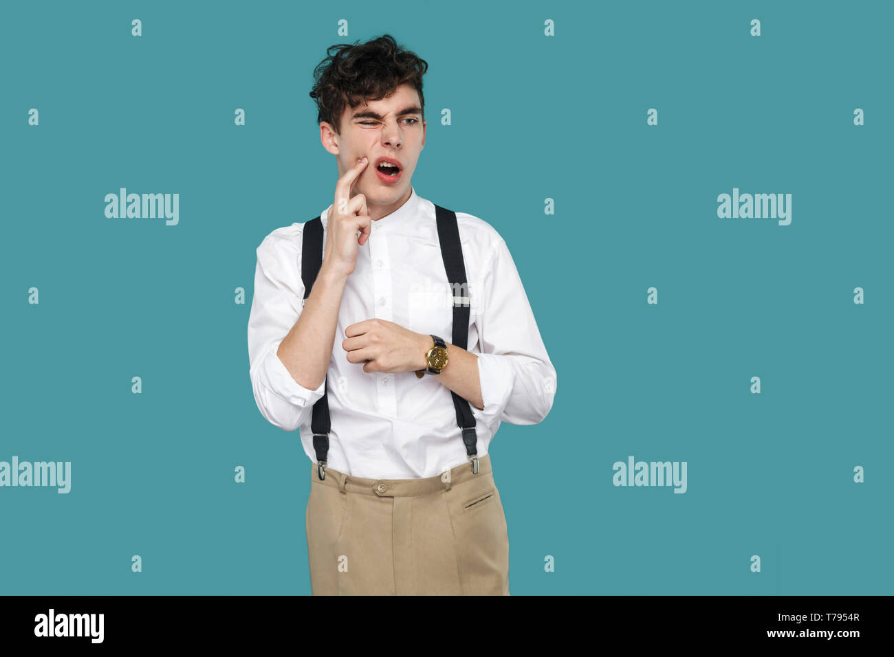 Tooth pain. man touching his chin because toothache. Portrait of handsome hipster curly young businessman in classic casual white shirt and suspender  Stock Photo