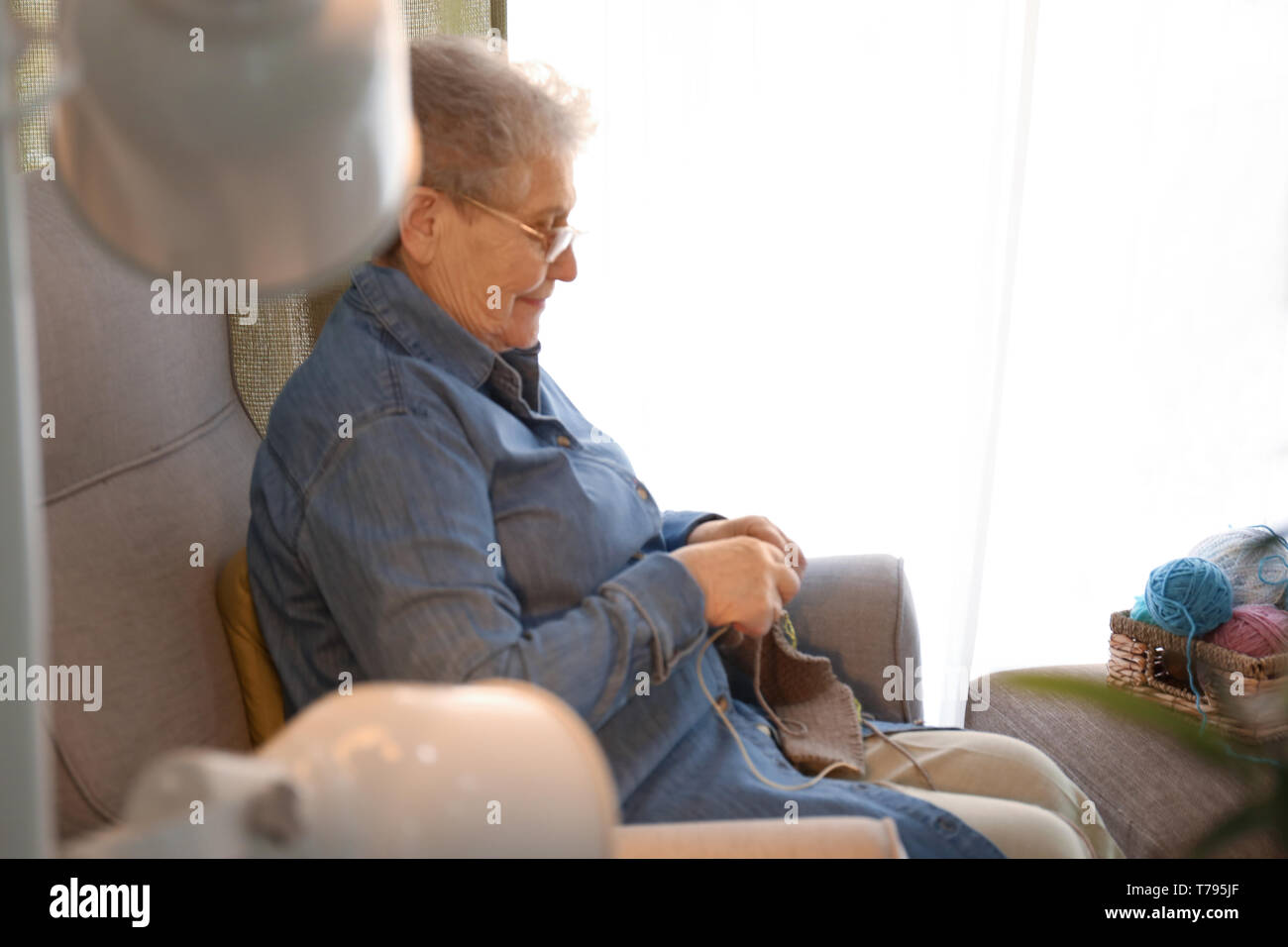 Senior woman sitting on armchair while knitting sweater at home Stock ...