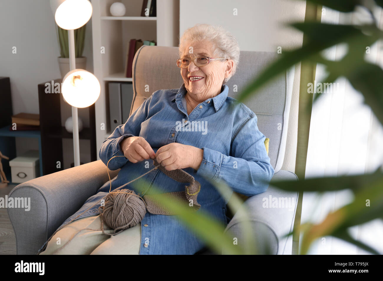 Senior woman sitting on armchair while knitting sweater at home Stock ...