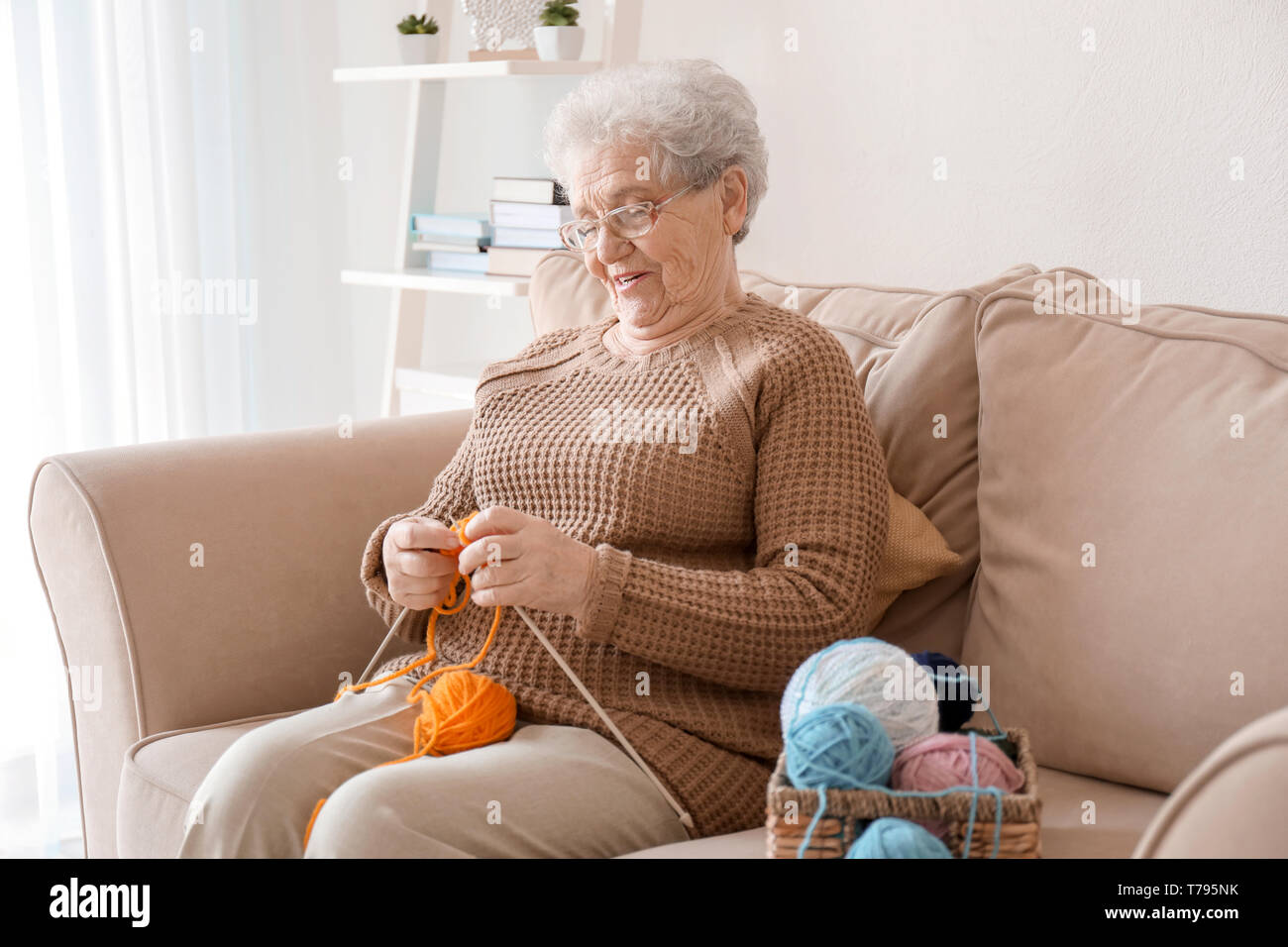 Senior woman sitting on sofa while knitting sweater at home Stock Photo ...
