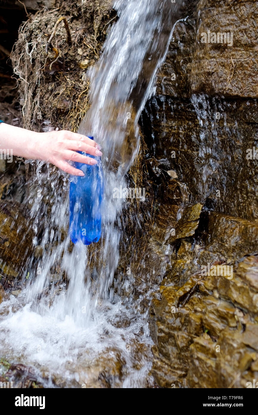 Woman holding a plastic bottle drawing clean water from cold spring ...