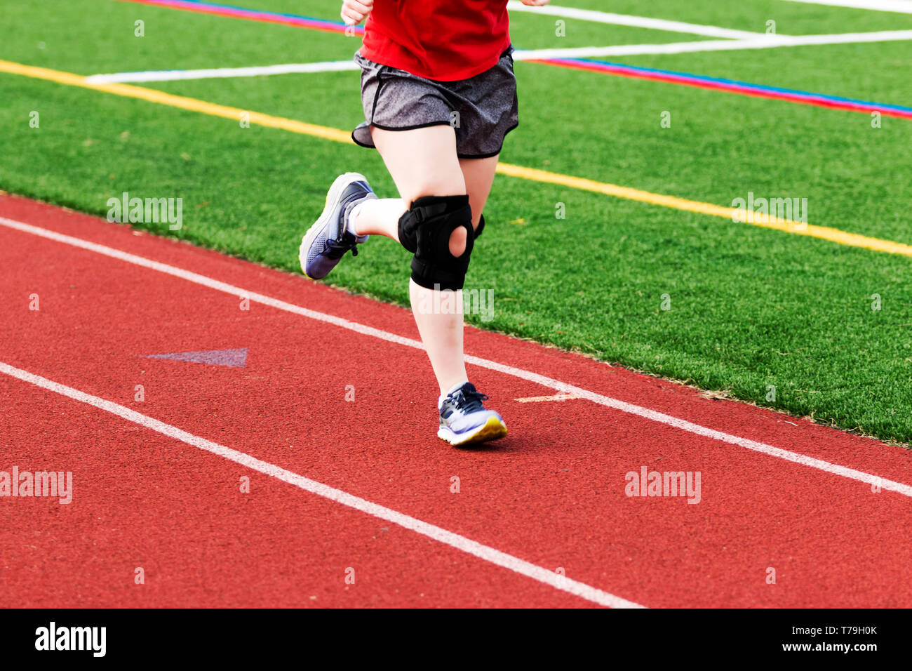 A runner is practicing on a red track while wearing a large black knee brace. Stock Photo