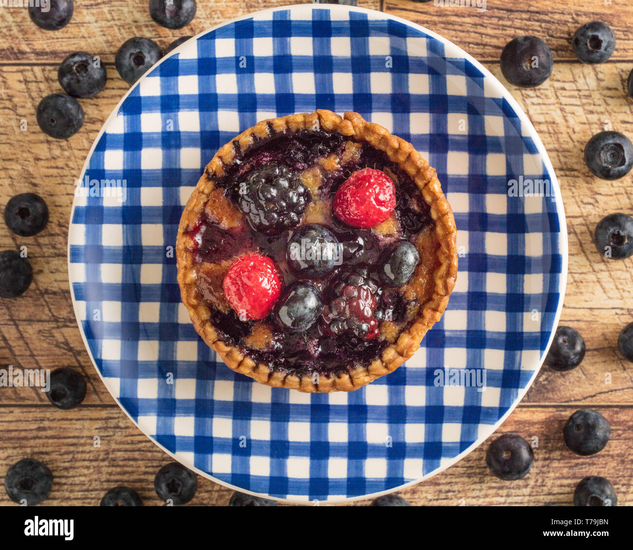 Mixed Berry Tart on a Blue Gingham Plate with a Wood Table Background Stock Photo