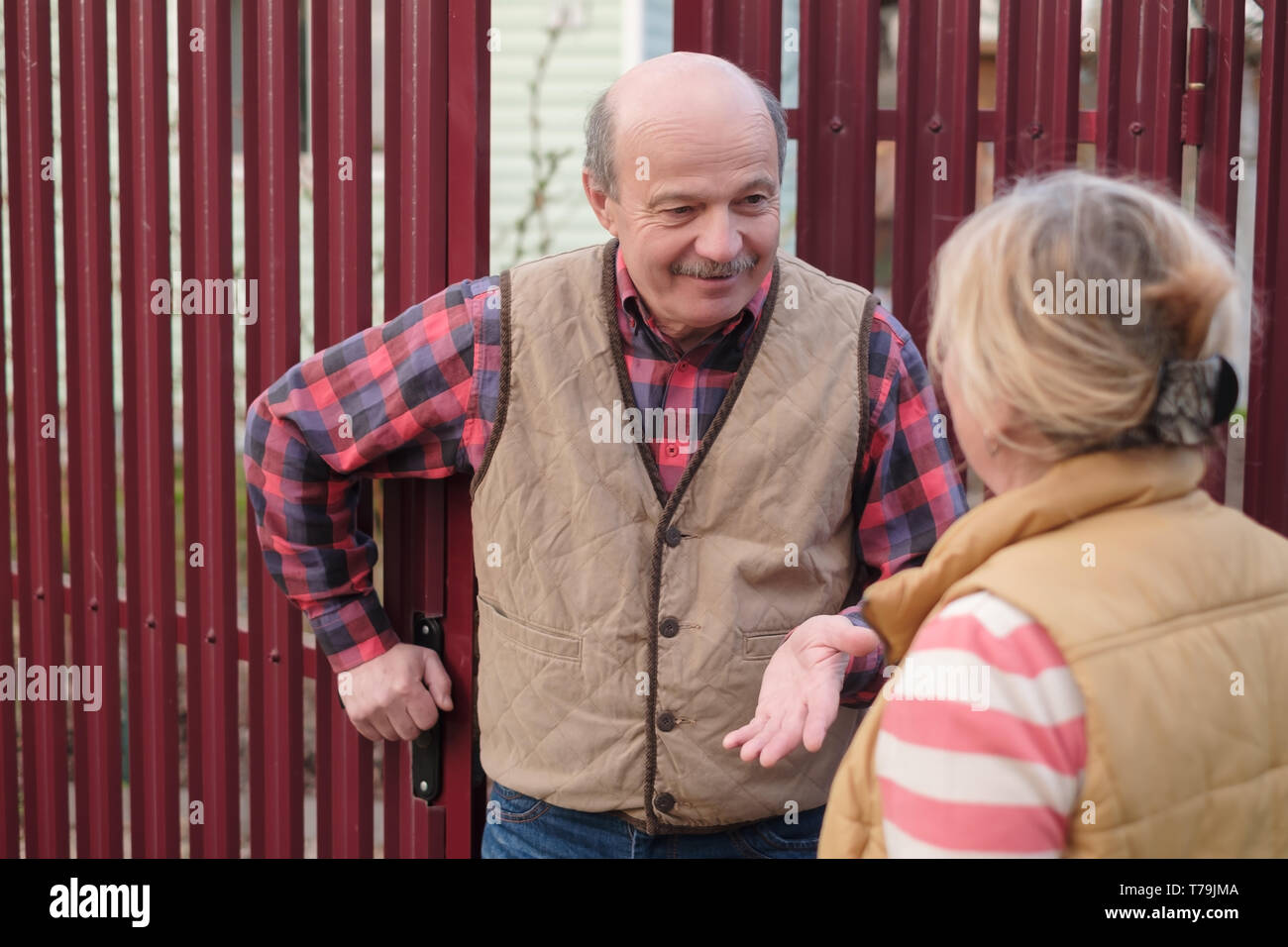 Two senior neighbors takling to each other on sunny day near fence. Stock Photo