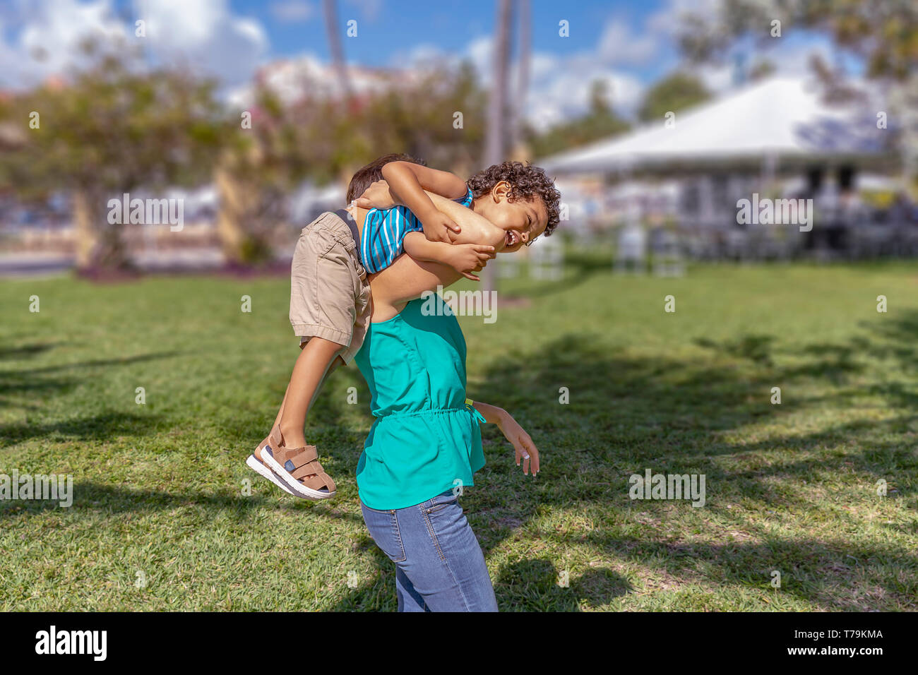 Mommy picks up the young toddler over her shoulder. He enjoys the outdoors with his mother laughing out loud as she walks with him on her shoulder. Stock Photo