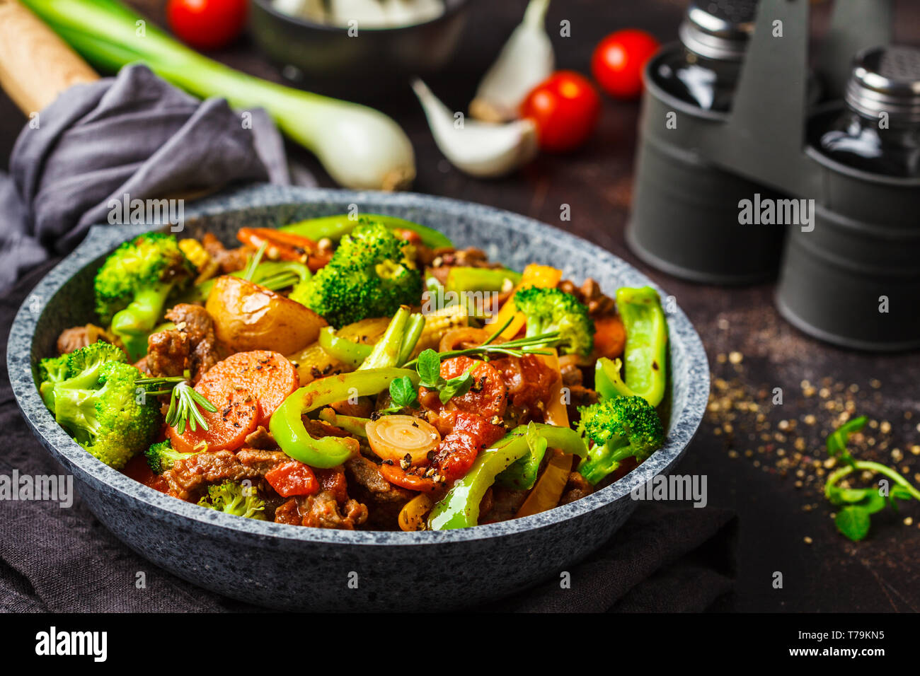 Fried beef stroganoff with potatoes, broccoli, corn, pepper, carrots and sauce in a pan, dark background. Stock Photo