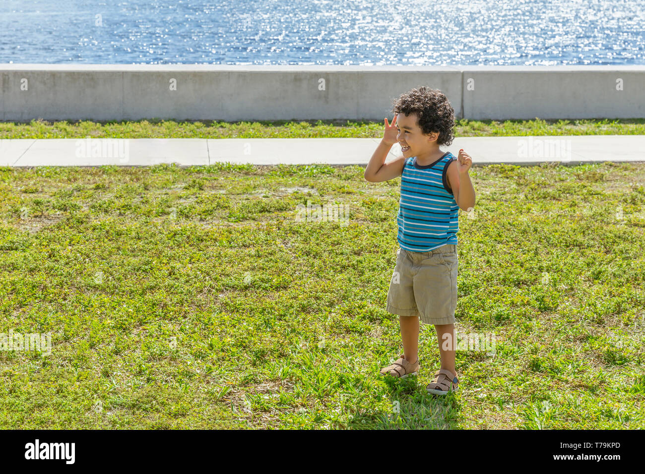 A little boy with hands in the air laughs as he plays. He enjoys the outdoors running around at the community park on the intercoastal. Stock Photo