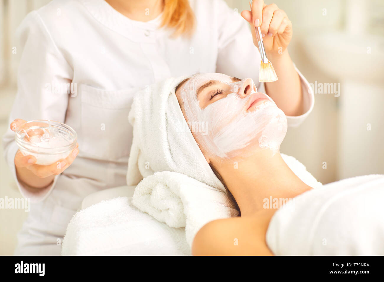 Beautician applies a white mask to a woman in the spa salon. Stock Photo