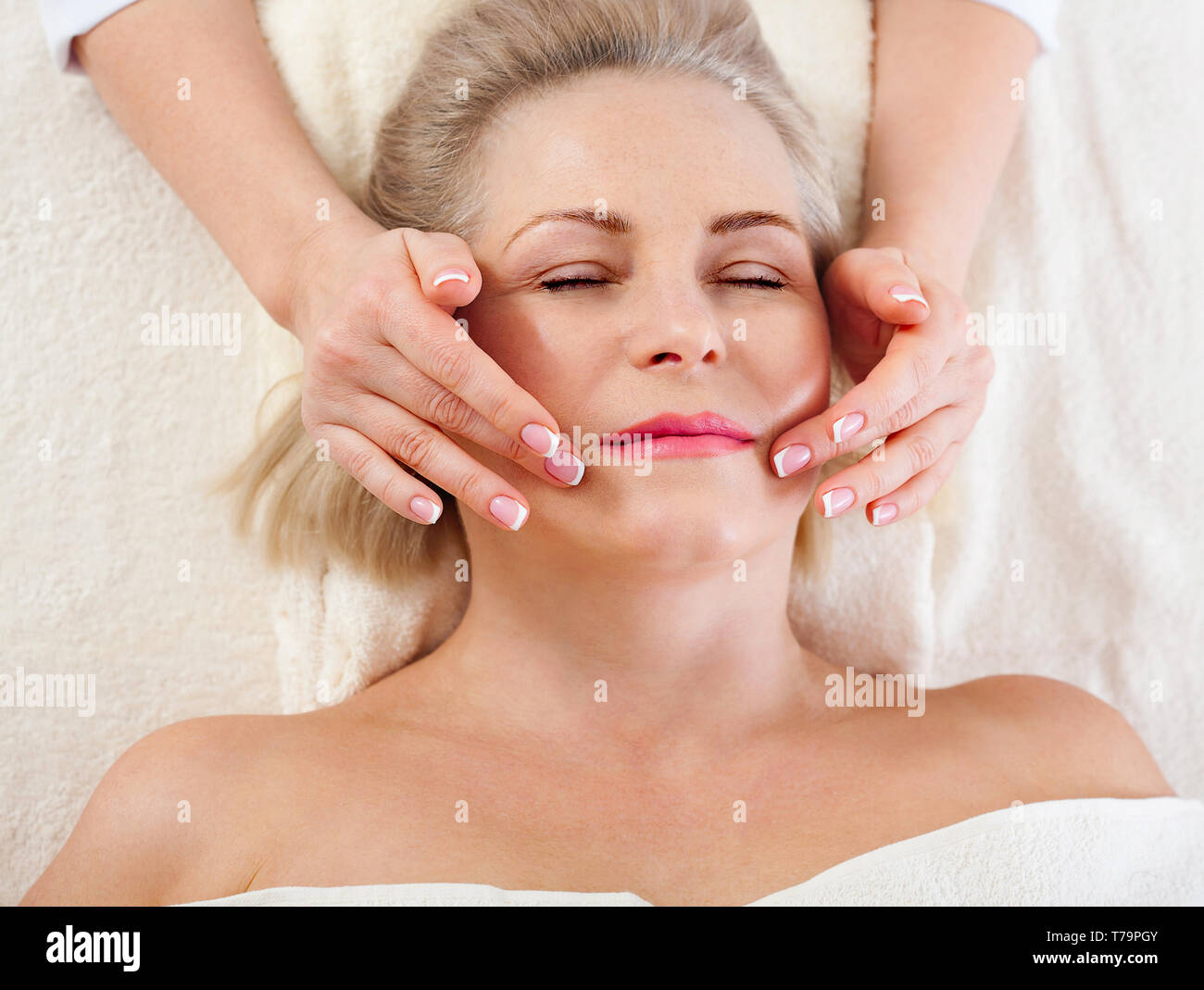 Face massage in spa environment macro. Attractive woman with close eyes taking skin care. Massage face selective focus. Stock Photo