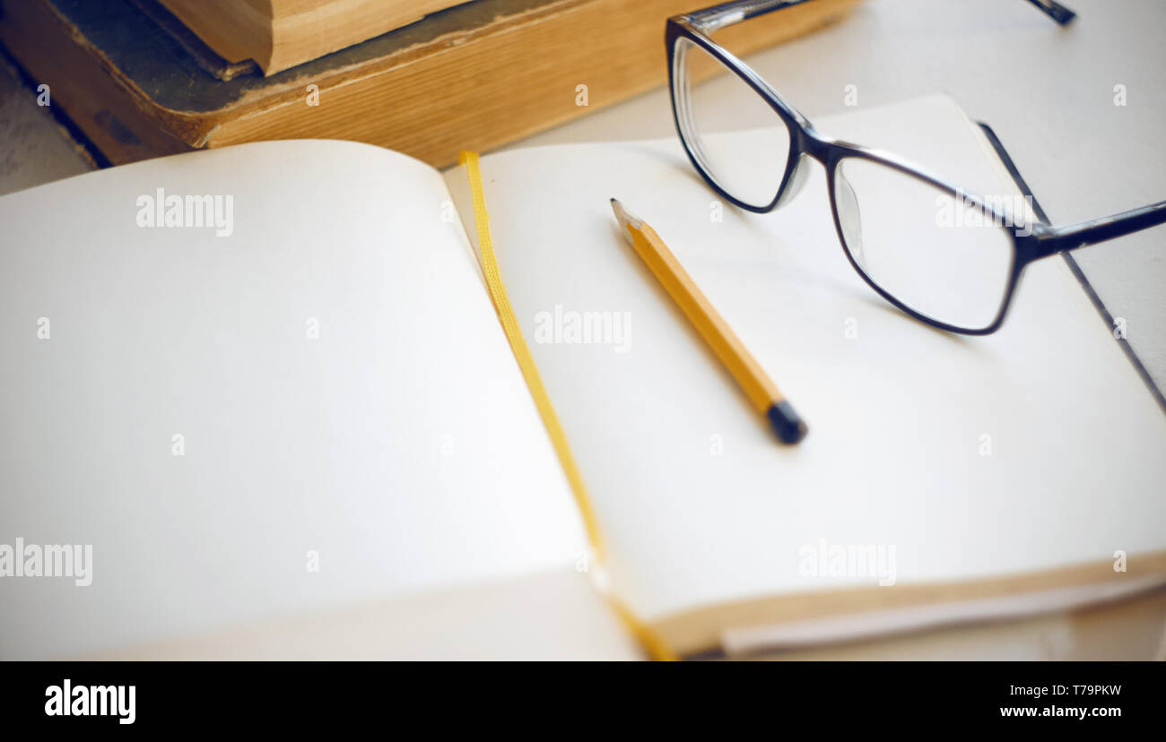 Things on the desktop that are needed to study the scientific material: ancient encyclopedias, notebook, yellow pencil and glasses Stock Photo
