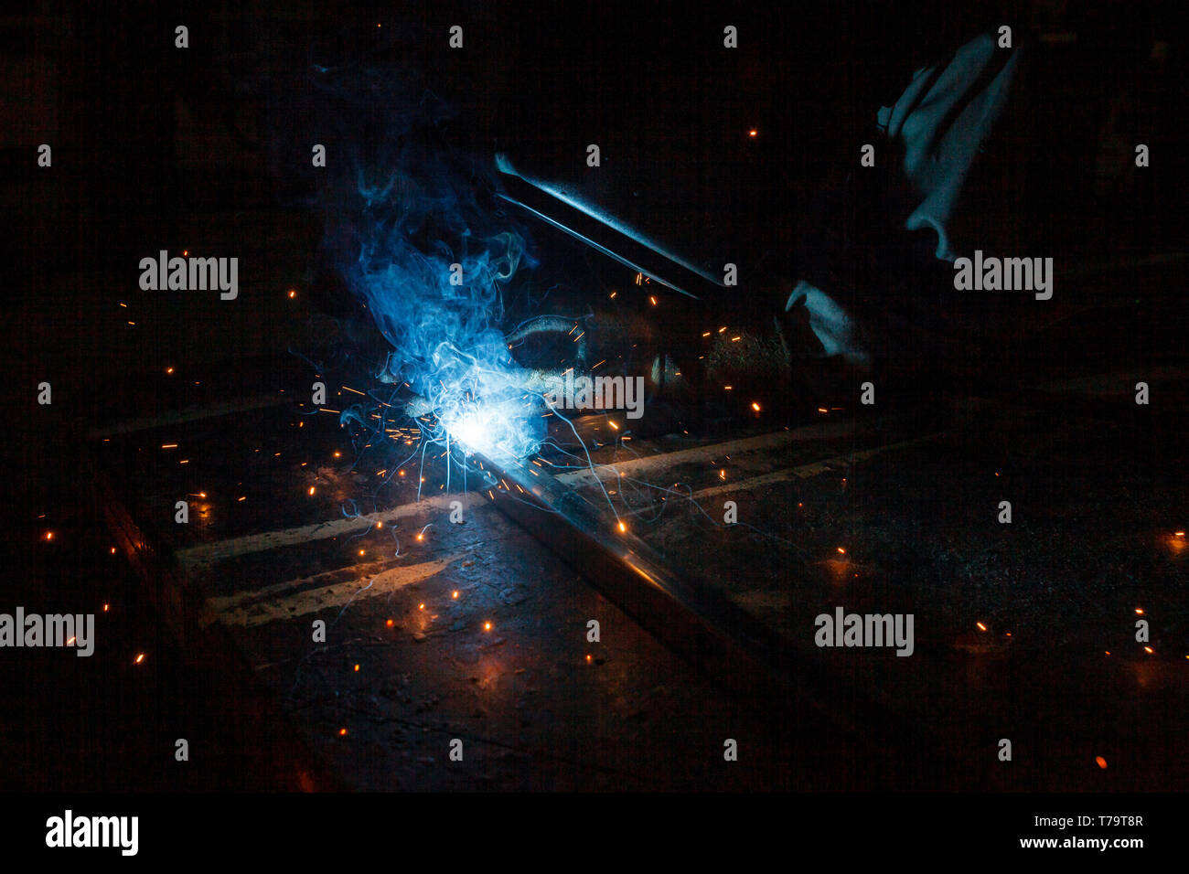 View of welding on construction site at night with shower of sparks and blue ark of electricity Stock Photo