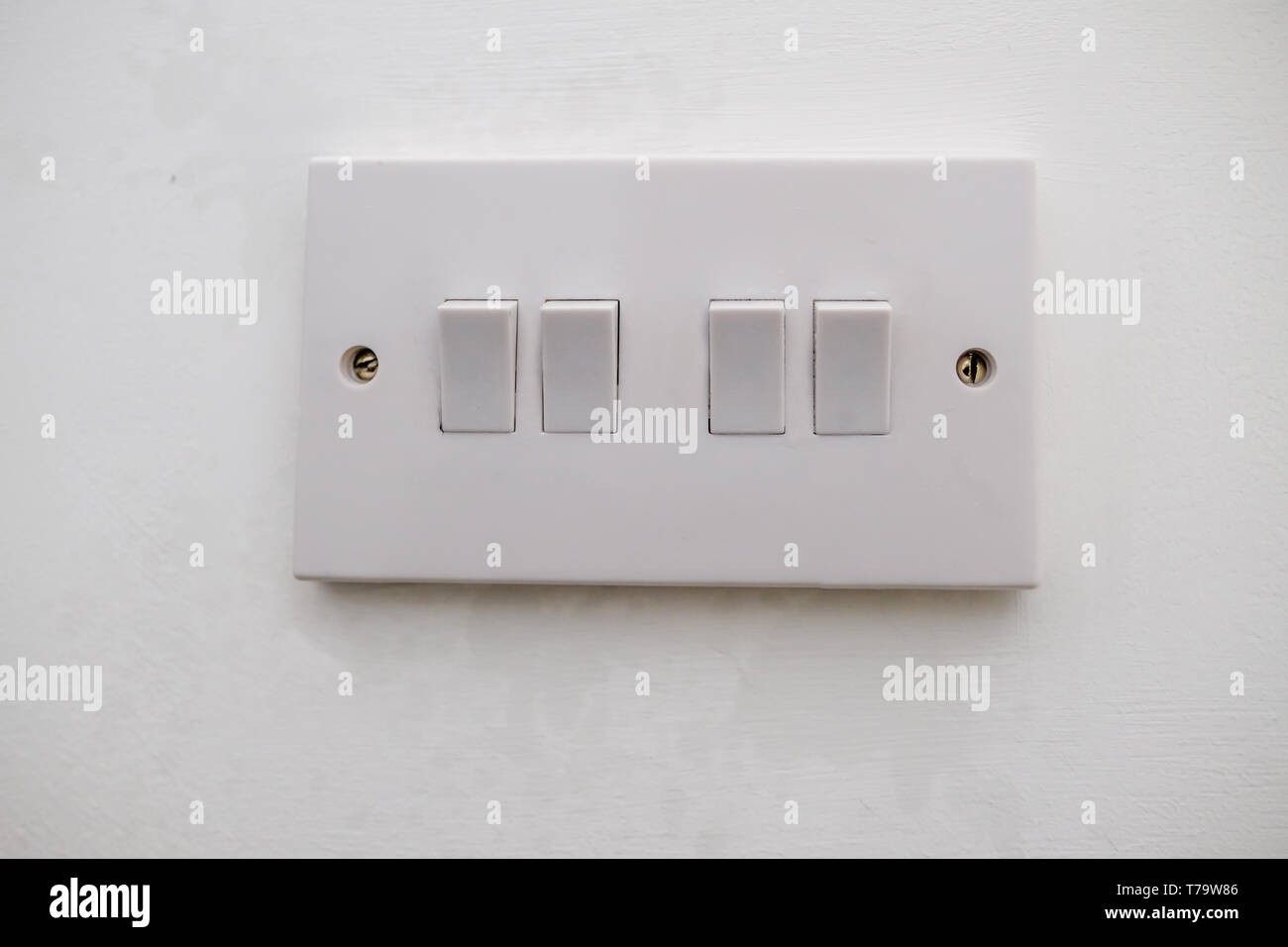 Four way electrical light switch.  White plastic switch with two screws and set agains a white painted wall. Stock Photo