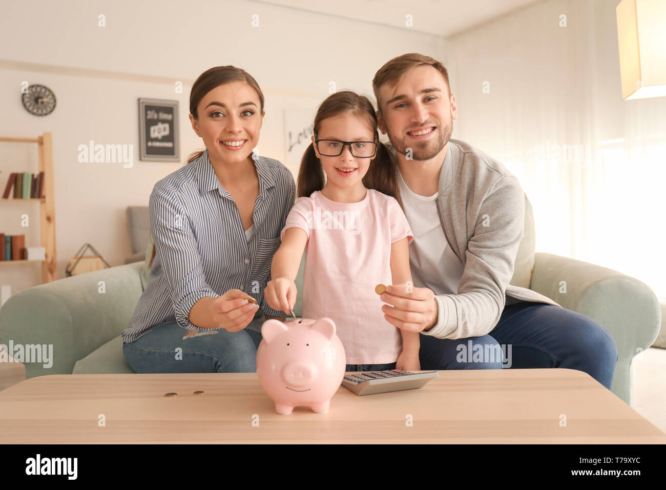 Happy little girl with her parents putting coins piggy into bank ...