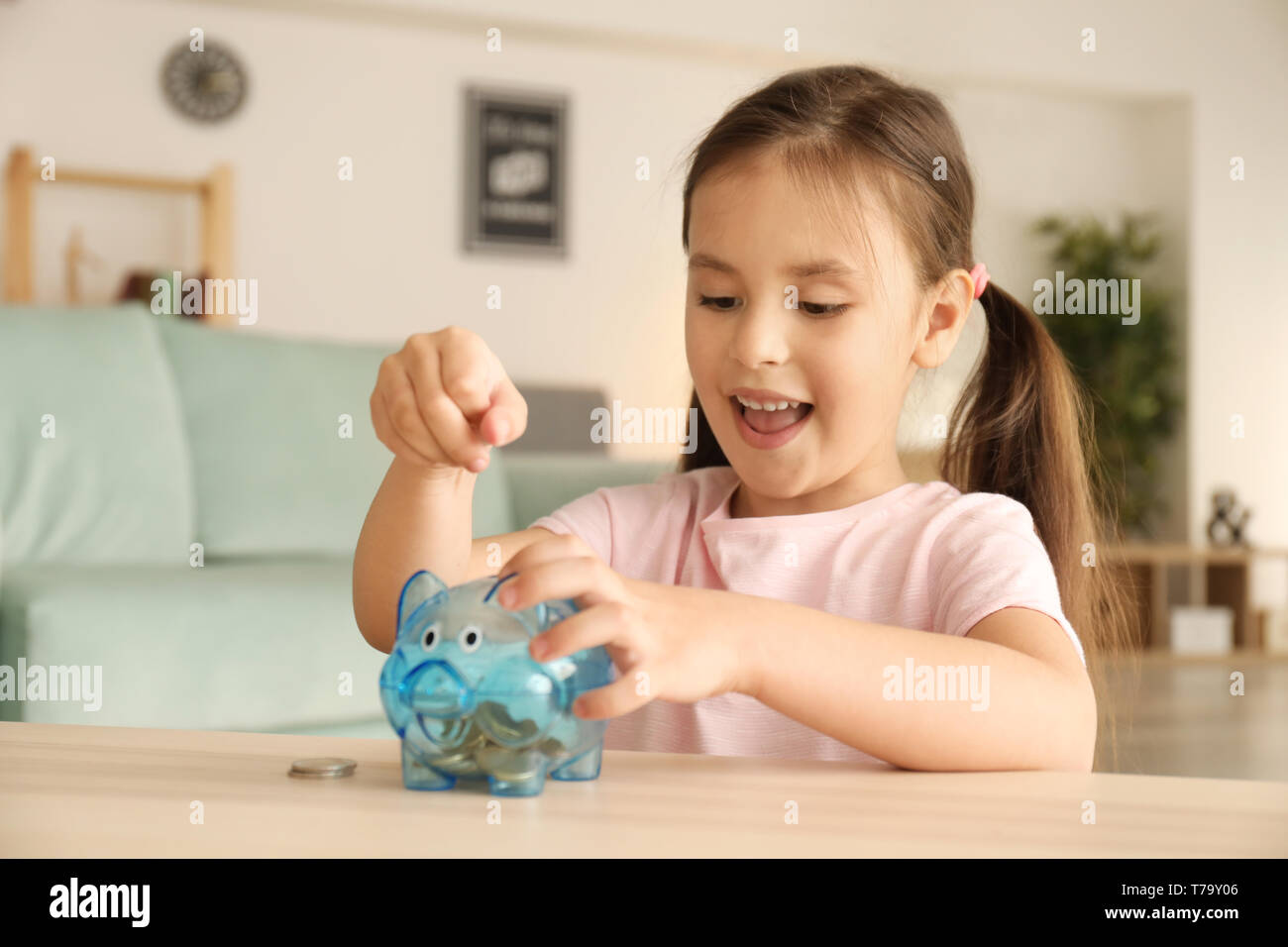 Little girl putting coins into piggy bank indoors. Money savings ...