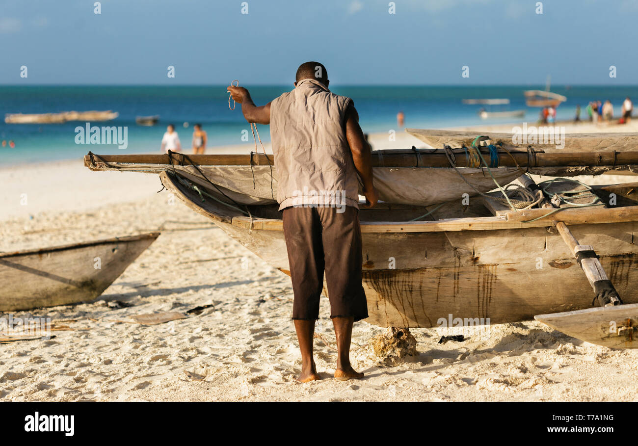 Poor African fisherman repairing his old wooden boat on the ocean Stock Photo